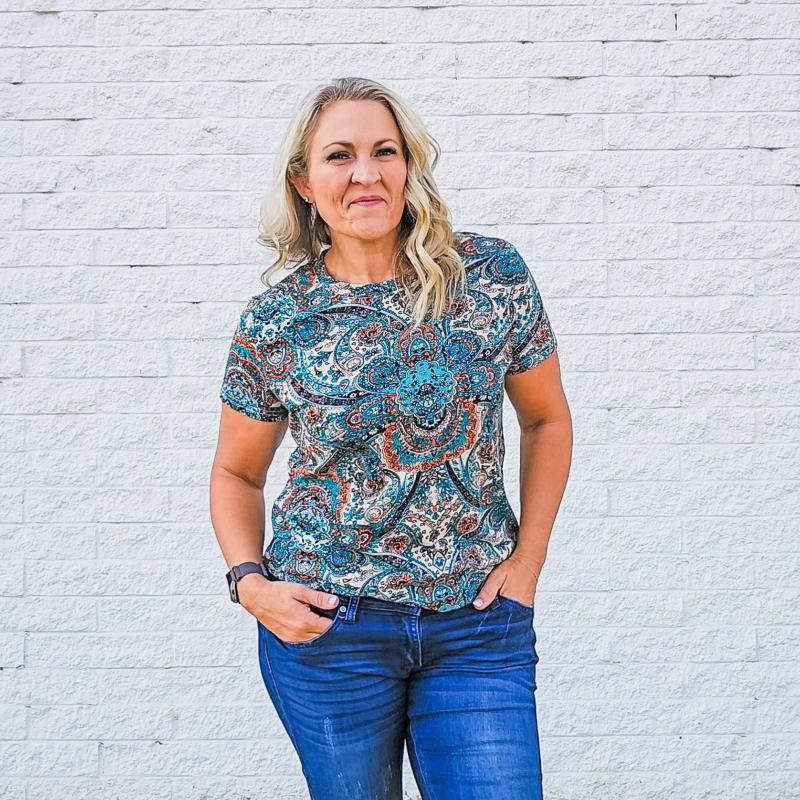 A woman wearing a short-sleeved paisley design shirt with a round neckline. shown in size medium