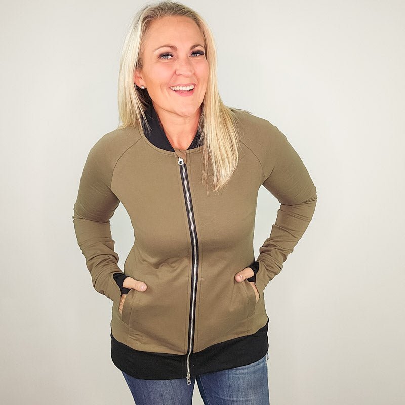 A woman wearing a green hoodless jacket with a stand collar, full front zipper, thumbholes, and watch cuff. shown in size medium