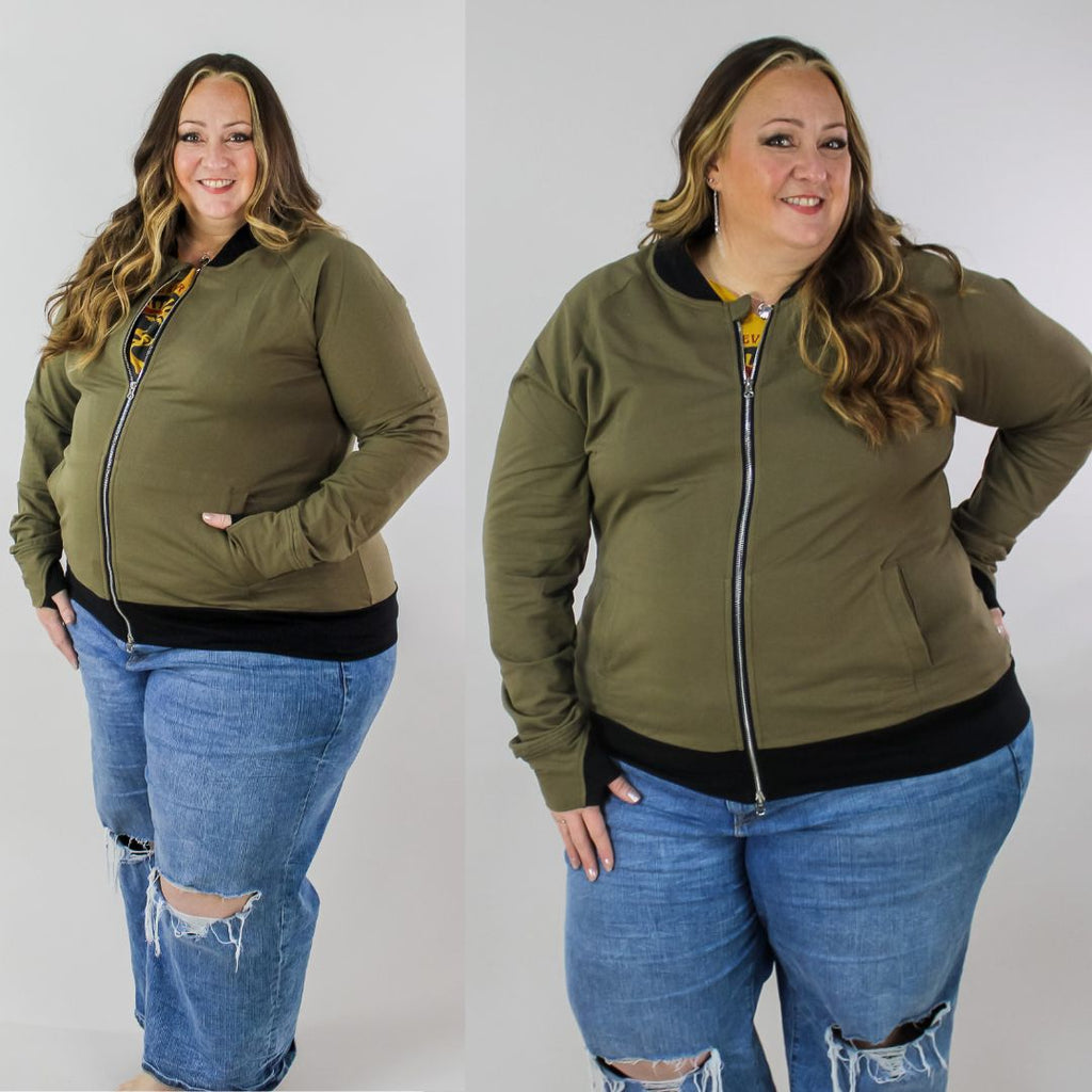 A woman wearing a green hoodless jacket with a stand collar, full front zipper, thumbholes, and watch cuff. shown in size 3XL