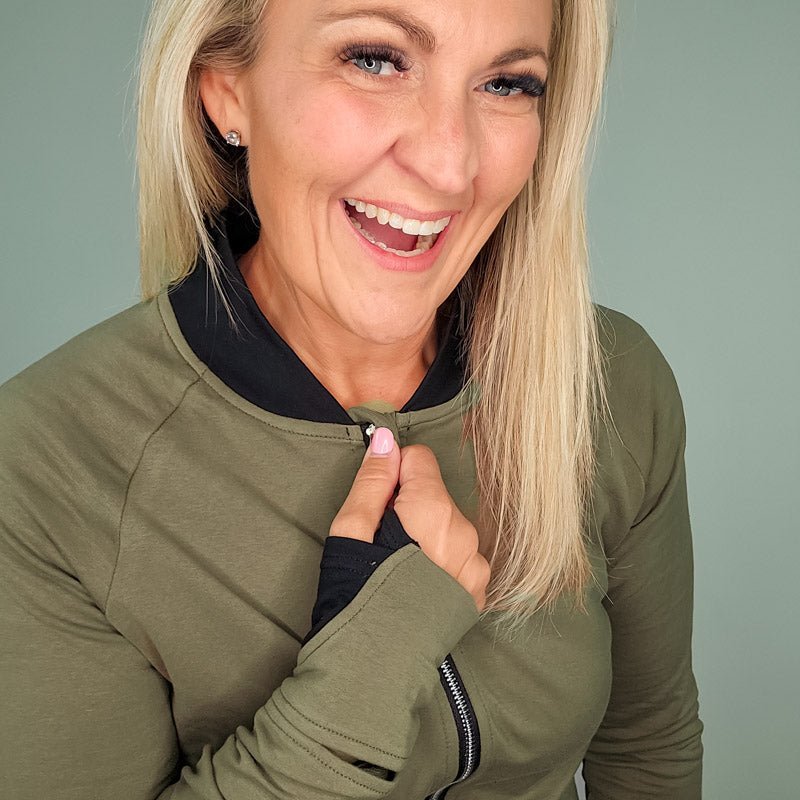 A woman wearing a green hoodless jacket with a stand collar, full front zipper, thumbholes, and watch cuff. shown in size medium