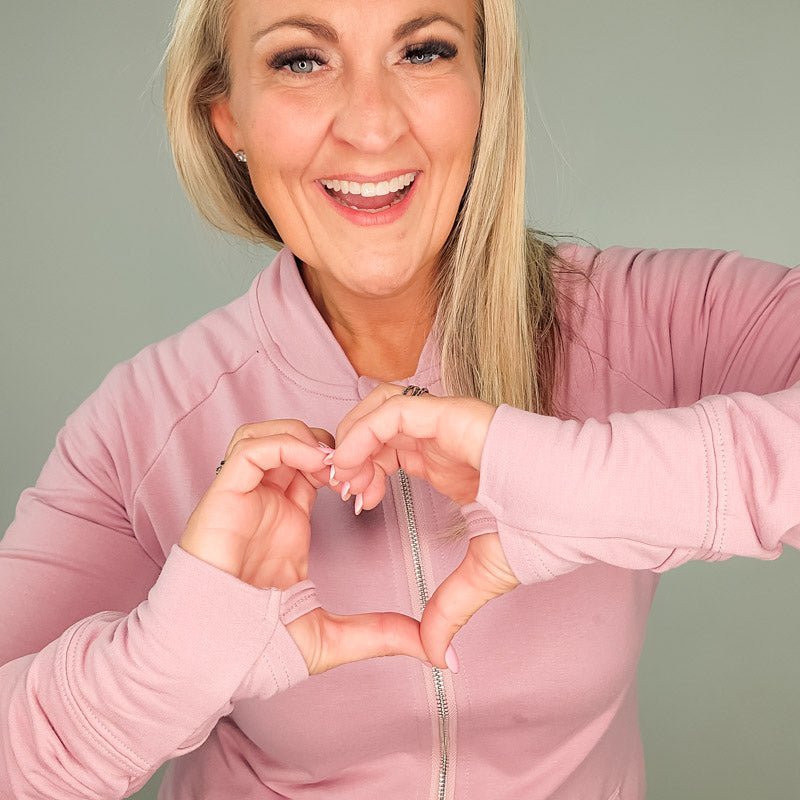 A woman wearing a pink hoodless jacket with a stand collar, full front zipper, and thumbholes. shown in size medium