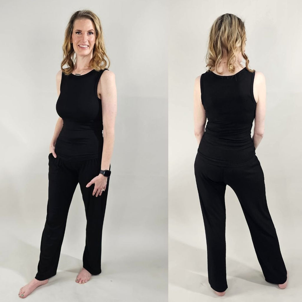 A woman wearing a black high-neck ribbed tank top. shown in size XS. paired with black ribbed wide leg pants. 