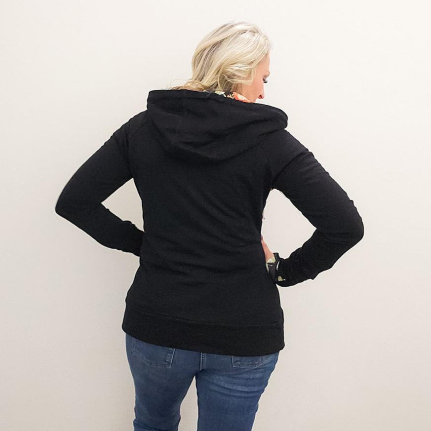 A woman wearing a black hoodie with a floral print on the front, featuring a half zip, floral print-lined hood and thumbholes, and kangaroo pocket. shown in size medium