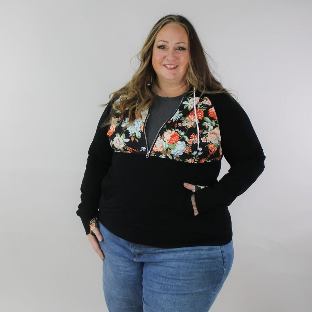 A woman wearing a black hoodie with a floral print on the front, featuring a half zip, floral print-lined hood and thumbholes, and kangaroo pocket. shown in size 3XL