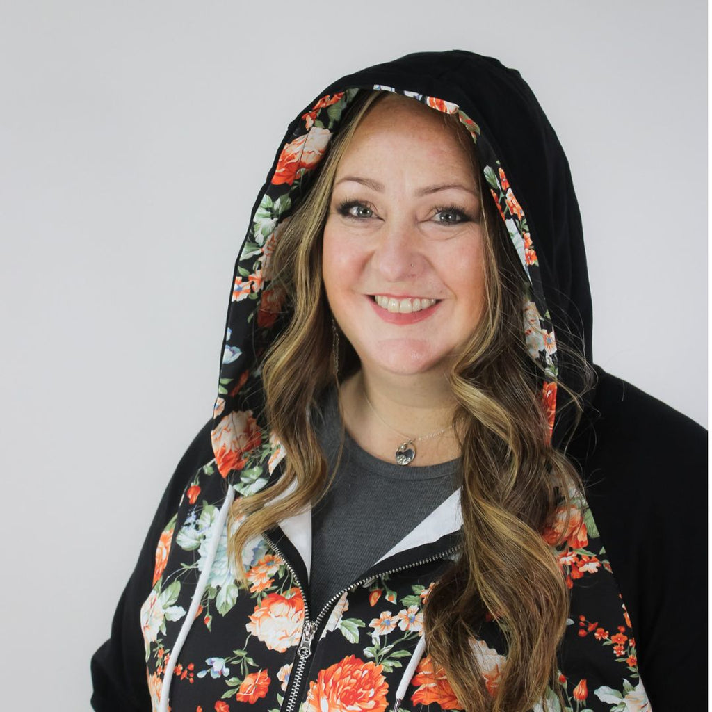 A woman wearing a black hoodie with a floral print on the front, featuring a half zip, floral print-lined hood and thumbholes, and kangaroo pocket. shown in size 3XL