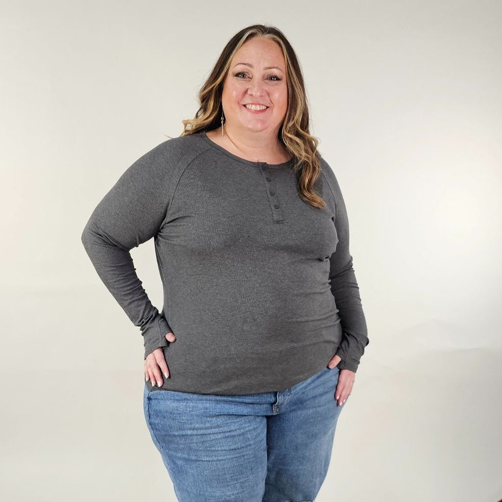 A woman wearing a dark grey long sleeve, semi-fitted, henley top with thumbholes. shown in size 3XL