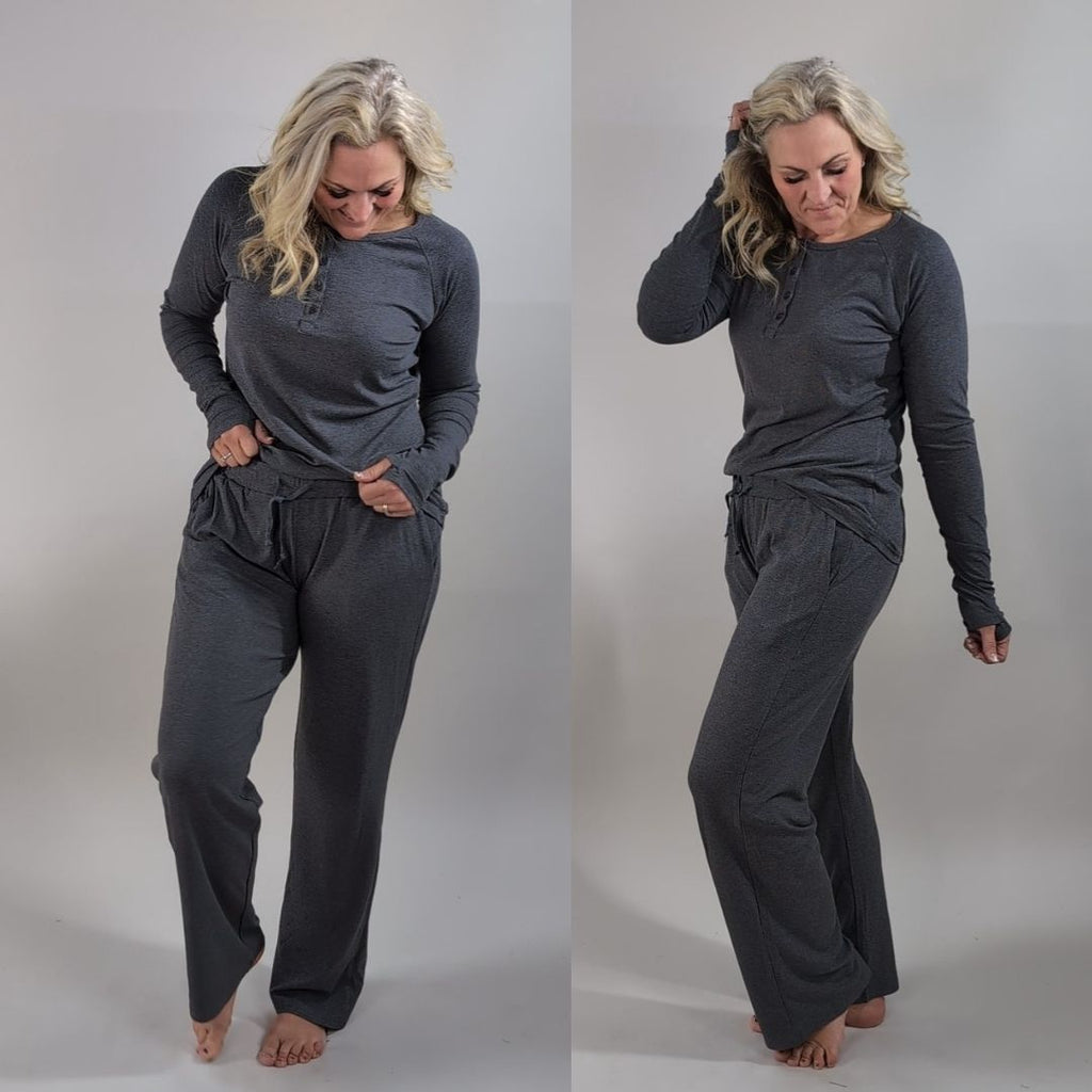A woman wearing a dark grey long sleeve, semi-fitted, henley top with thumbholes. shown in size medium. paired with dark grey ribbed wide leg pants in size medium. 