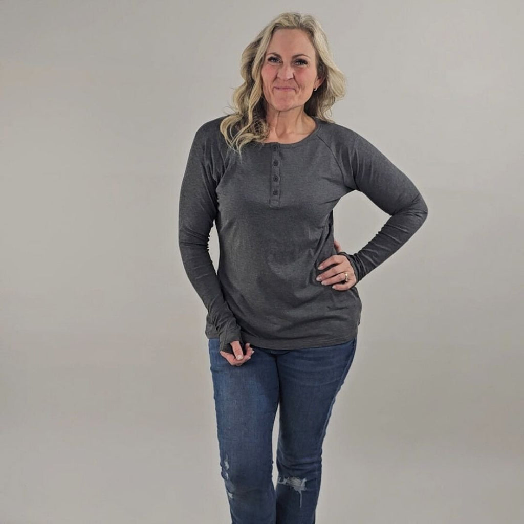 A woman wearing a dark grey long sleeve, semi-fitted, henley top with thumbholes. shown in size medium