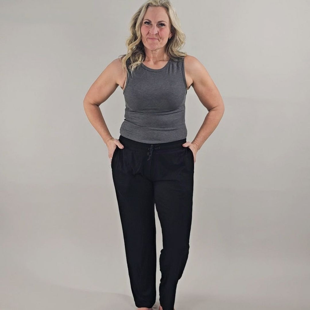 A woman wearing a dark grey ribbed high neck tank top and black ribbed pants. shown in size medium
