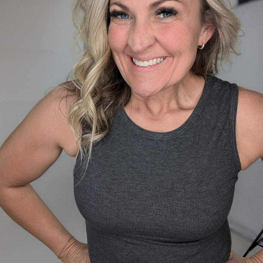 A woman wearing a dark grey ribbed high neck tank top. shown in size medium