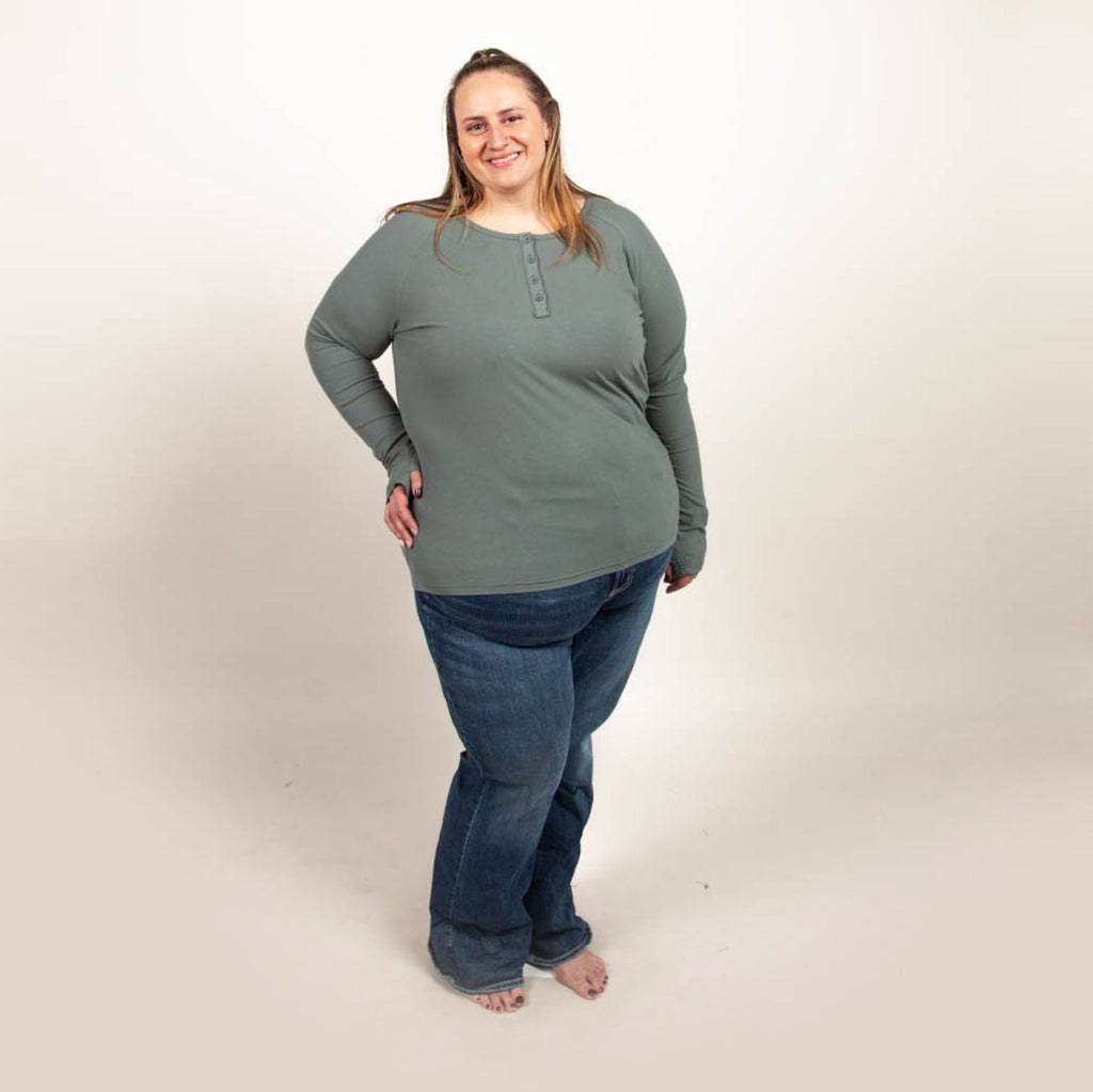 A woman wearing a dark sage long sleeve, semi-fitted, henley top with thumbholes. shown in size 2XL