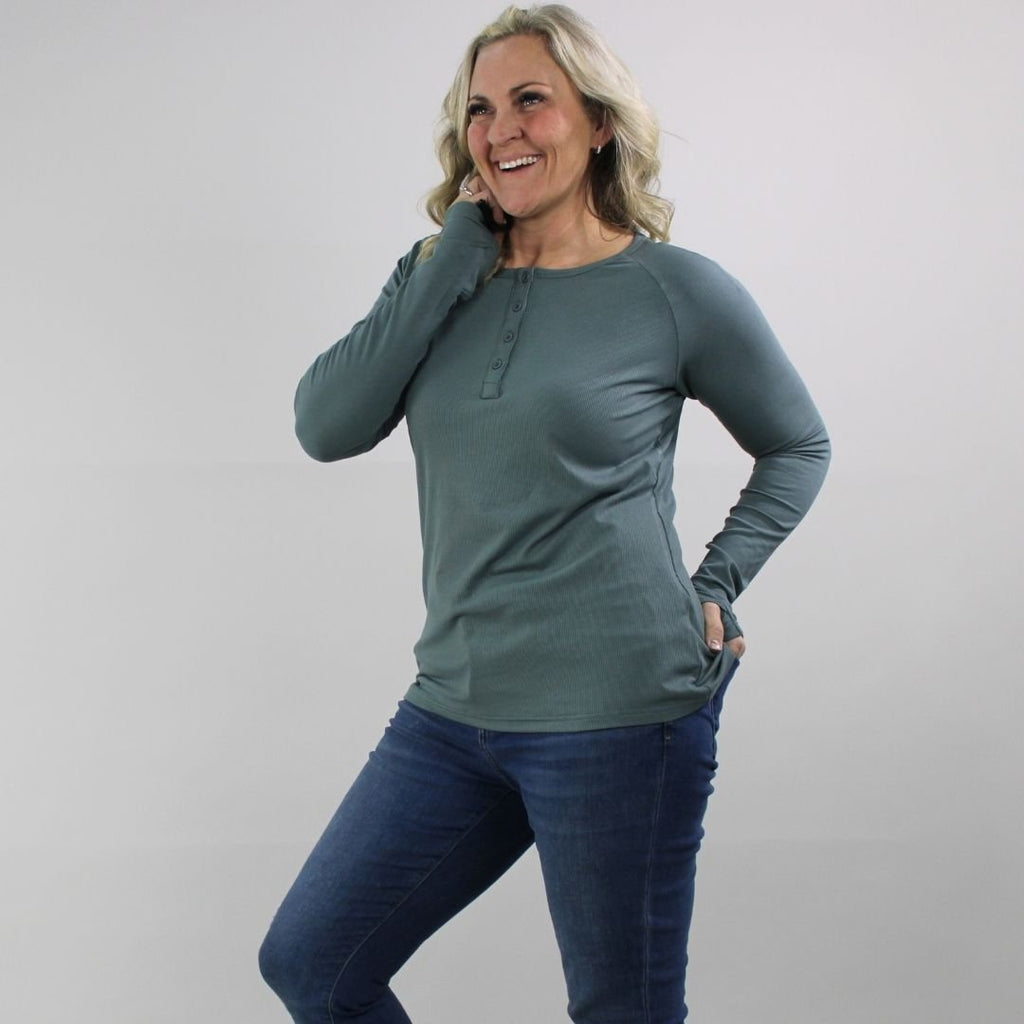 A woman wearing a dark sage long sleeve, semi-fitted, henley top with thumbholes. shown in size medium