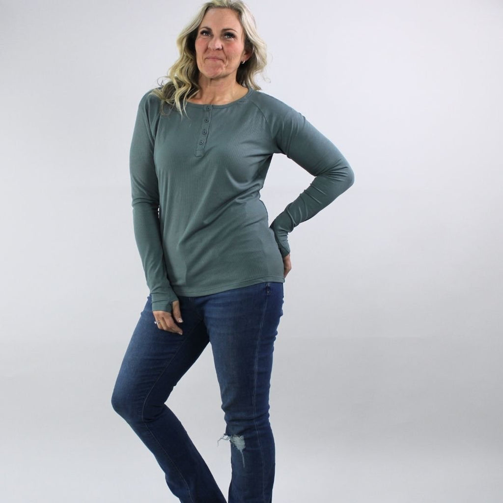 A woman wearing a dark sage long sleeve, semi-fitted, henley top with thumbholes. shown in size medium