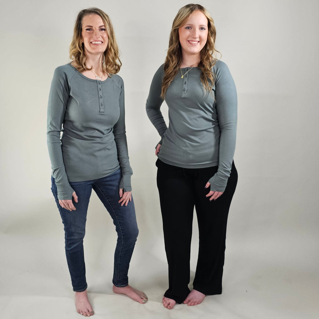 Two women wearing a dark sage long sleeve, semi-fitted, henley top with thumbholes. shown in size XS (left) and small (right). paired with black ribbed wide leg pants in size large (right). 
