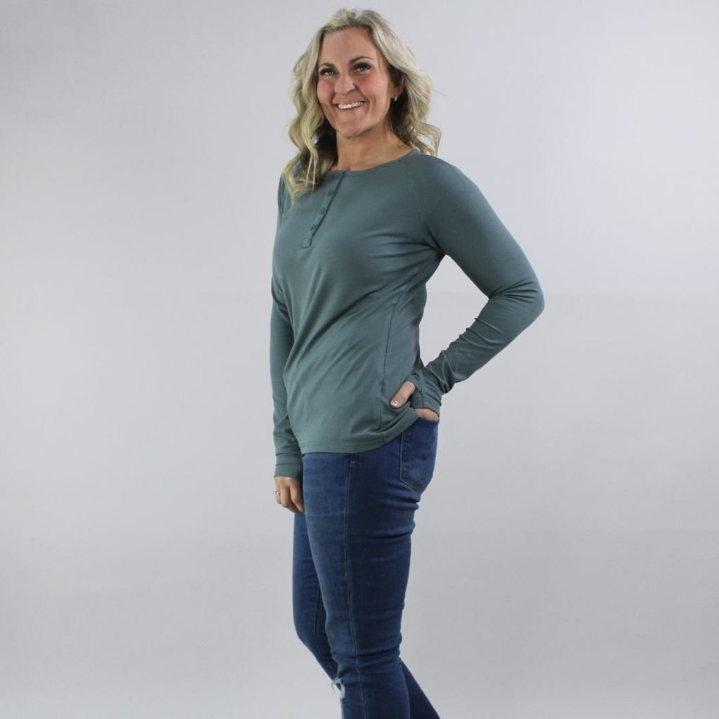 A woman wearing a dark sage long sleeve, semi-fitted, henley top with thumbholes. shown in size medium