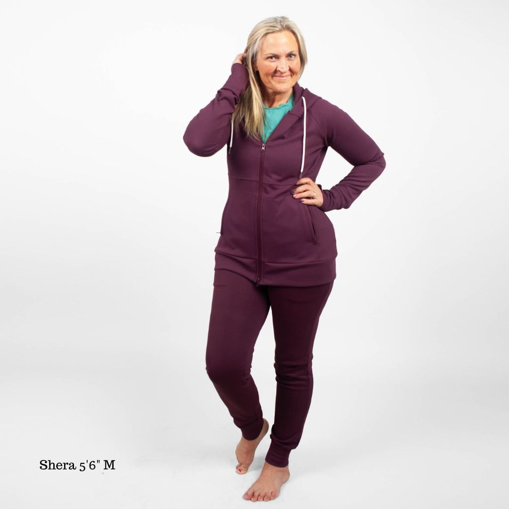 A woman standing, wearing  Eggplant Scuba Joggers 31" Inseam with a wide elastic waistband and tapered ankle cuffs, shown in size medium womens. paired with an Eggplant Scuba Full Zip  hoodie