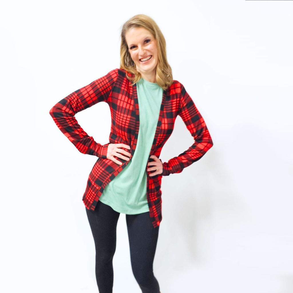 A woman smiling and posing in a red and black plaid cardigan with tailored cuffs and thumbholes. shown in size XS