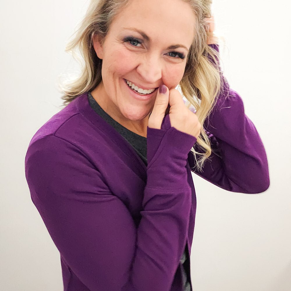 A woman wearing a purple open cardigan with long sleeves and thumbholes - shown in size medium. paired with a grey top 