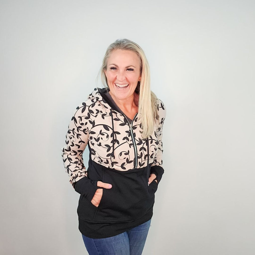 Woman wearing a black and beige patterned hoodie, half zip, kangaroo pocket, and thumbholes. shown in size medium