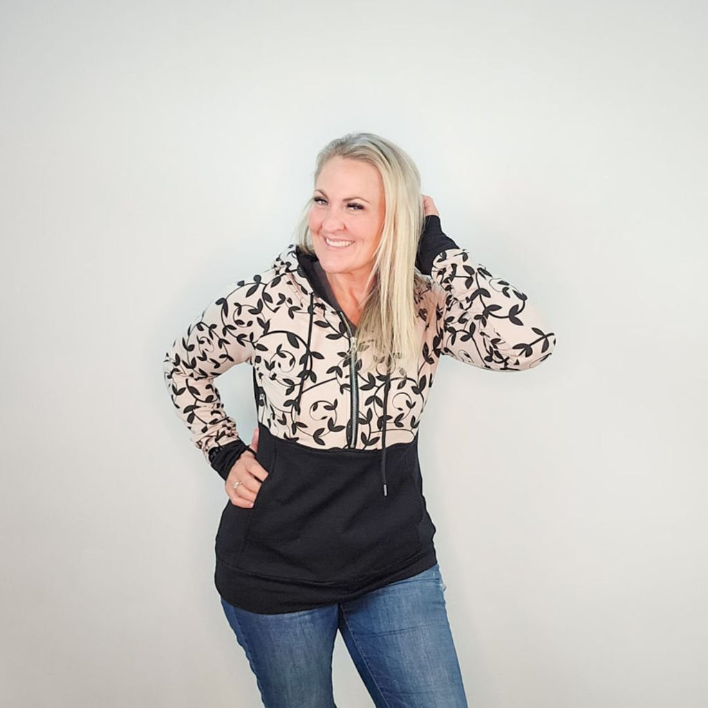 Woman wearing a black and beige patterned hoodie, half zip, kangaroo pocket, and thumbholes. shown in size medium