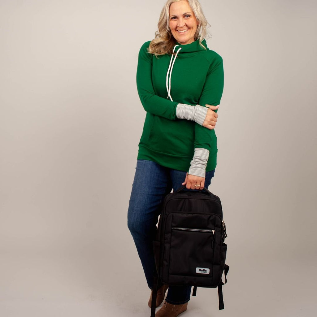 Go-Be by 7degrees backpack – stylish and functional travel bag for women or men. Lightweight and easy to carry with top handle. Woman wearing green hoodie holding black backpack by top handle.