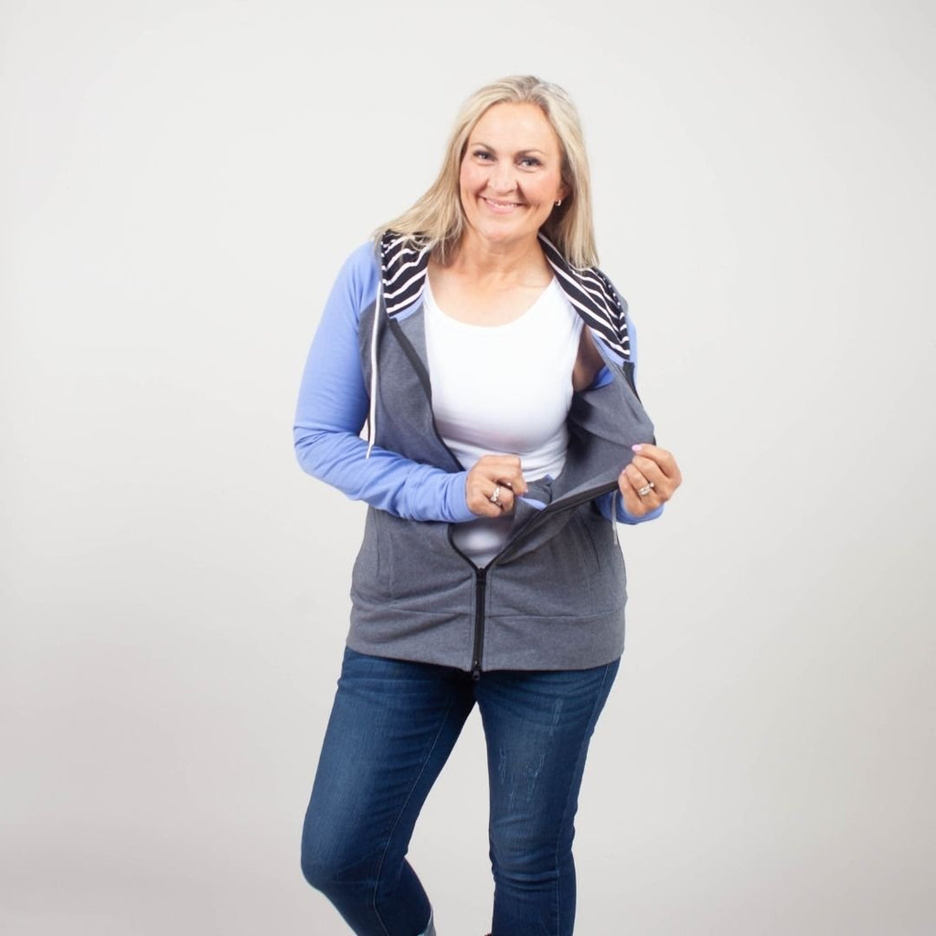Woman wearing a gray and blue hoodie with side pockets, inside pocket, and a black and white striped pattern on the hood and thumbholes. shown in size medium