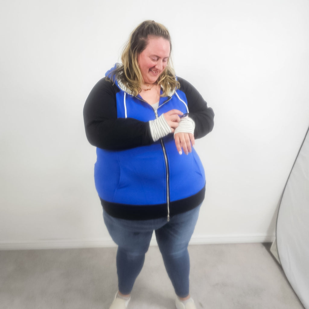 Woman wearing a blue and black hoodie with a white and black pinstripe lined hood with thumbholes and full double zipper.  features watch cuff. shown in size 3XL