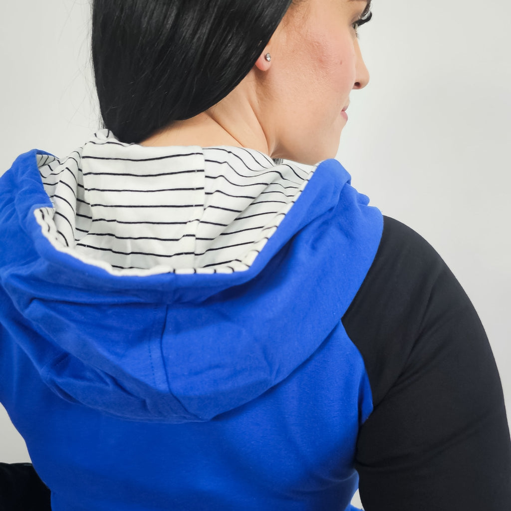 Woman wearing a blue and black hoodie with a white and black pinstripe lined hood with thumbholes and full double zipper.  features watch cuff. shown in size small