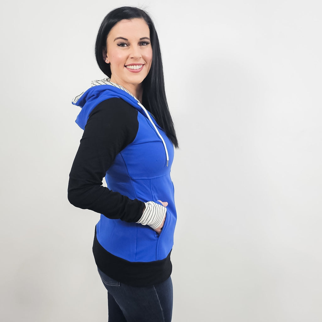 Woman wearing a blue and black hoodie with a white and black pinstripe lined hood with thumbholes and full double zipper.  features watch cuff. shown in size small