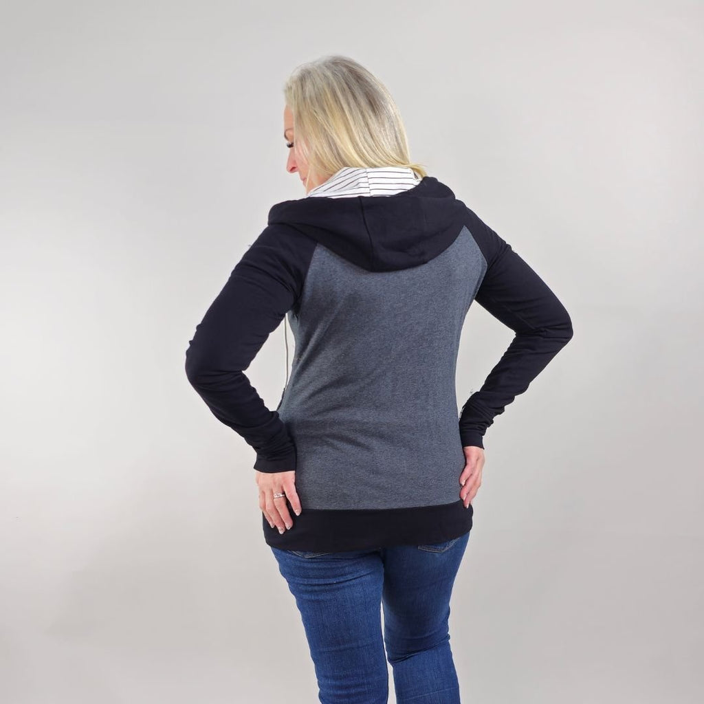 A woman wearing a dark gray hoodie with black sleeves and white pinstripes on the hood and thumb holes. shown in size medium