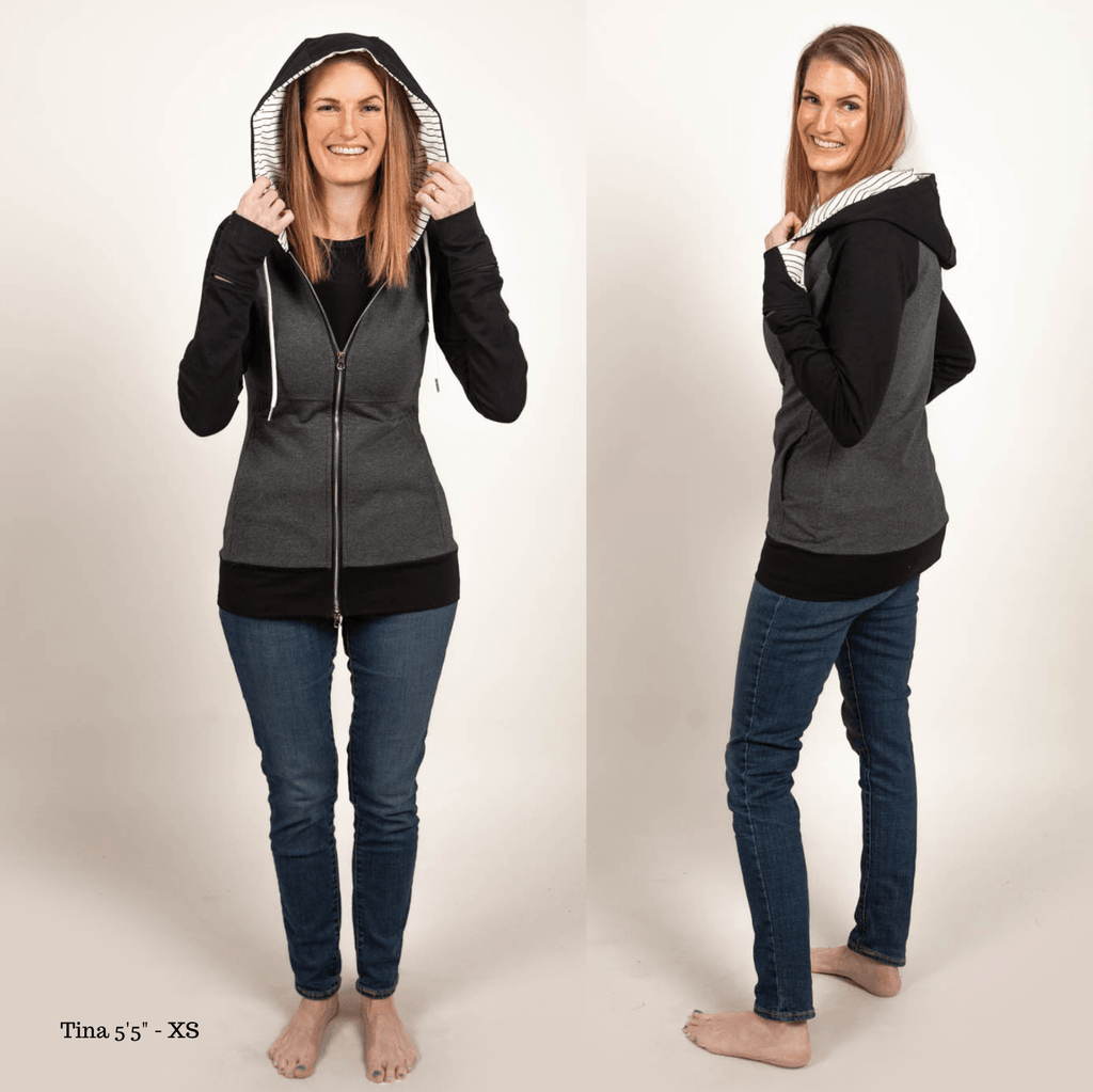 A woman wearing a dark gray hoodie with black sleeves and white pinstripes on the hood and thumb holes. shown in size XS