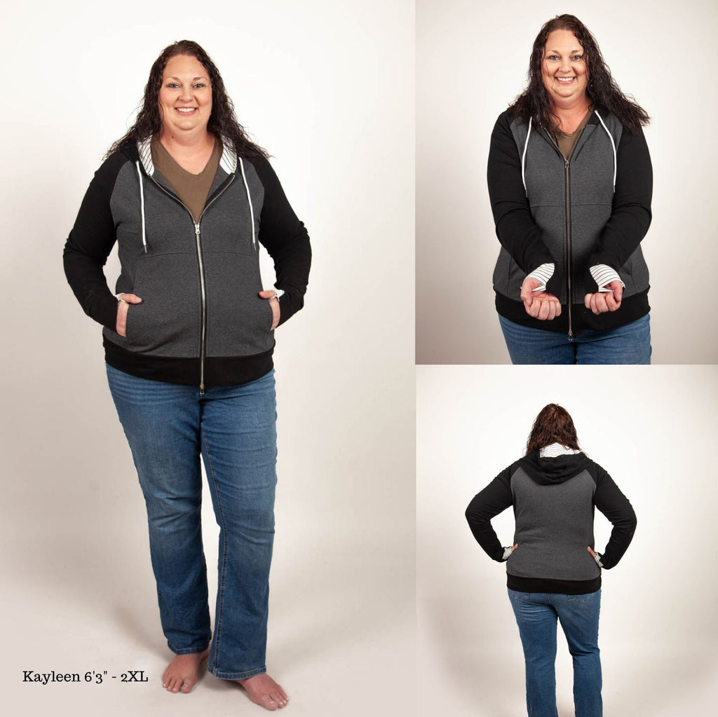 A woman wearing a dark gray hoodie with black sleeves and white pinstripes on the hood and thumb holes. shown in size 2XL