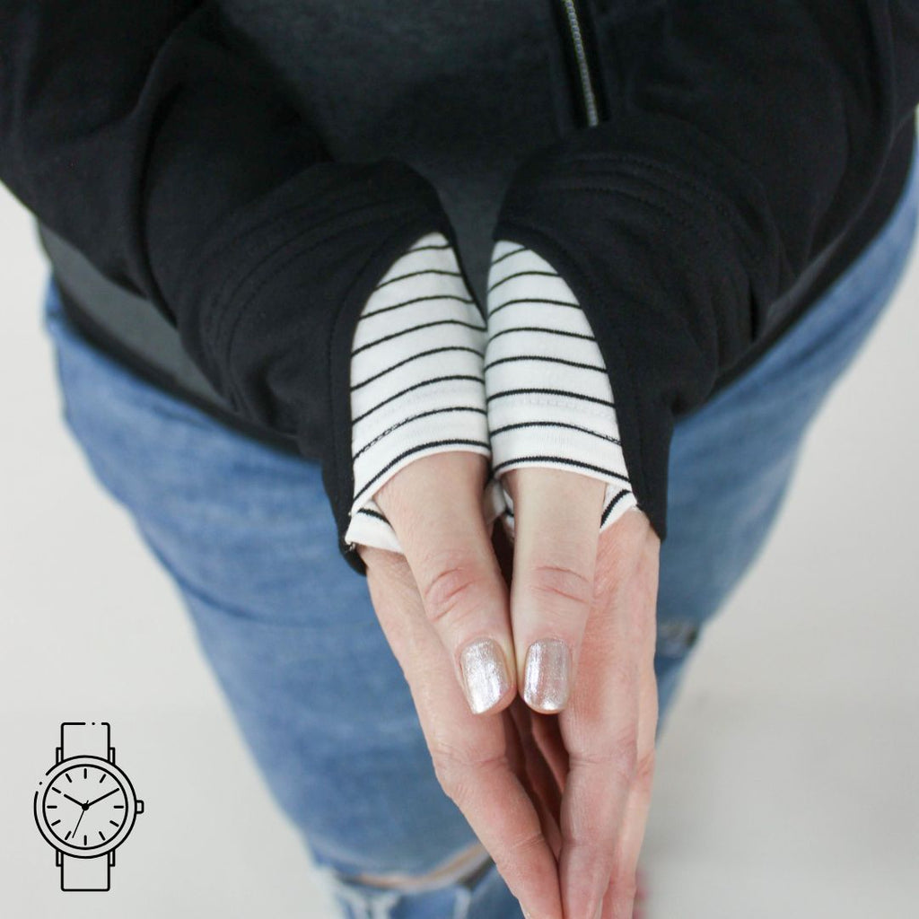 A woman wearing a dark gray hoodie showing detail of black sleeves and white pinstripes on thumb holes. 