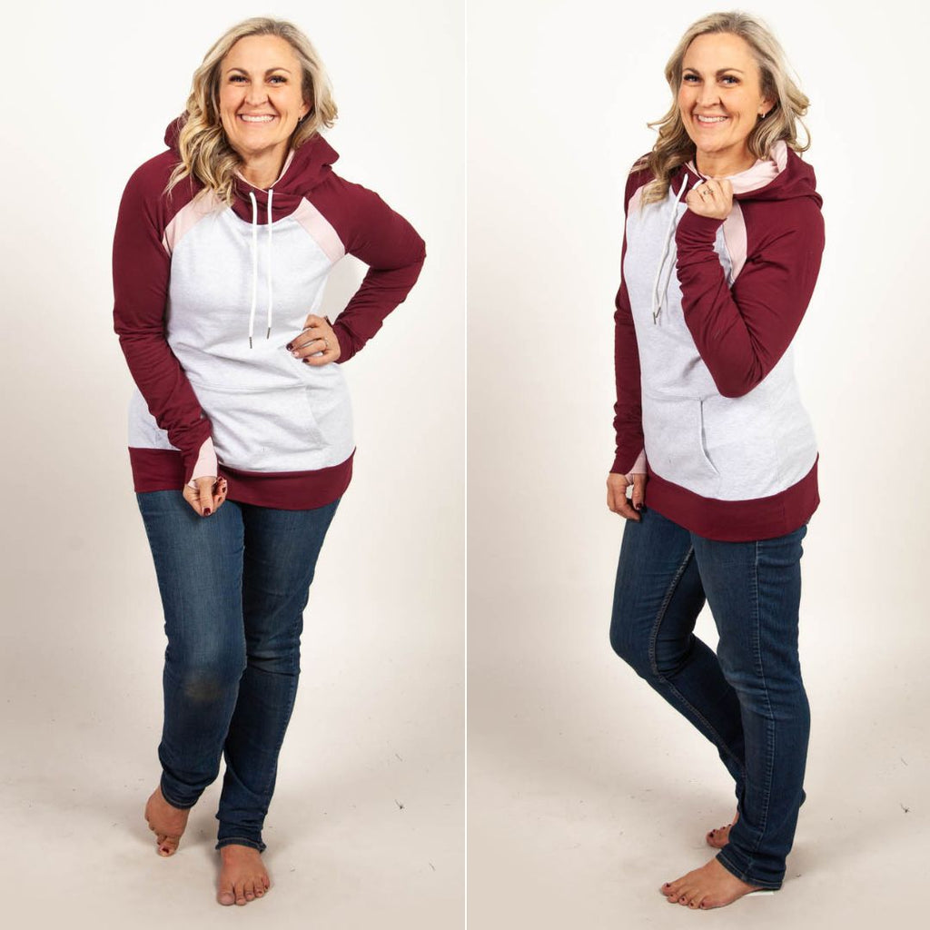 A woman wearing a two-tone hoodie with a burgundy color block design, featuring a hood, thumbholes, and a kangaroo pocket. shown in size medium