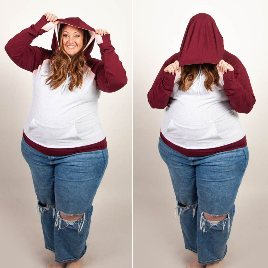 A woman wearing a two-tone hoodie with a burgundy color block design, featuring a hood, thumbholes, and a kangaroo pocket. shown in size 3XL