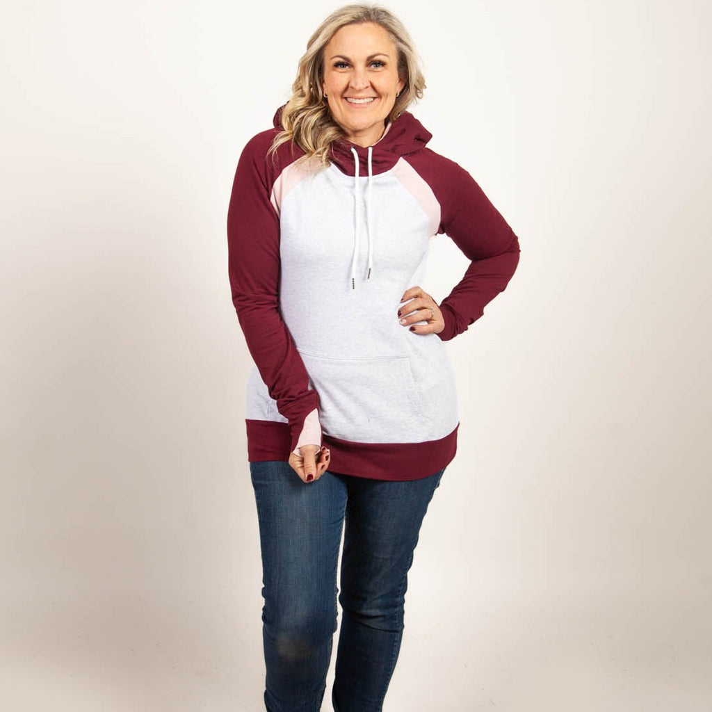 A woman wearing a two-tone hoodie with a burgundy color block design, featuring a hood, thumbholes, and a kangaroo pocket. shown in size medium