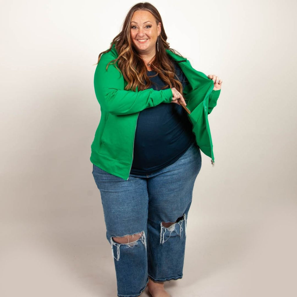 A woman wearing a green full zip hoodie with a hood, thumbholes, and a two-way zipper. shown in size 3XL