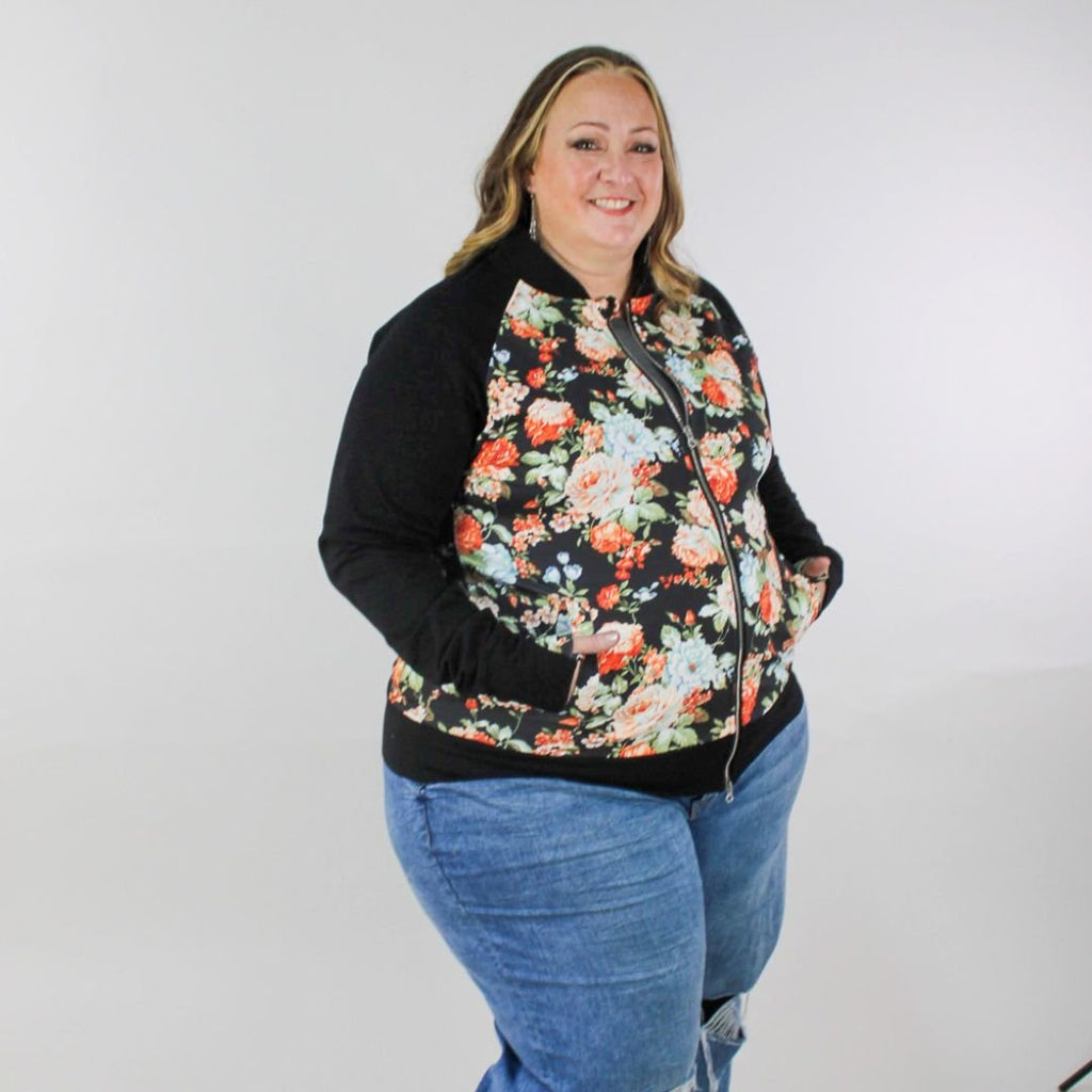 A woman wearing a floral print hoodless jacket with a stand collar, full front zipper, black sleeves, and floral  thumbholes. shown in size 3XL