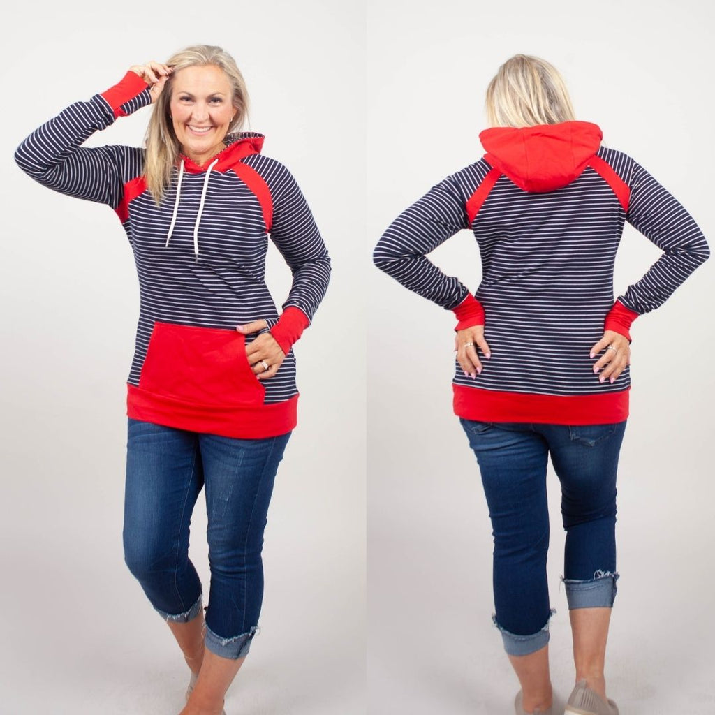 Woman wearing a blue and white striped hoodie with red accents, kangaroo pocket, and thumbholes. shown in size medium