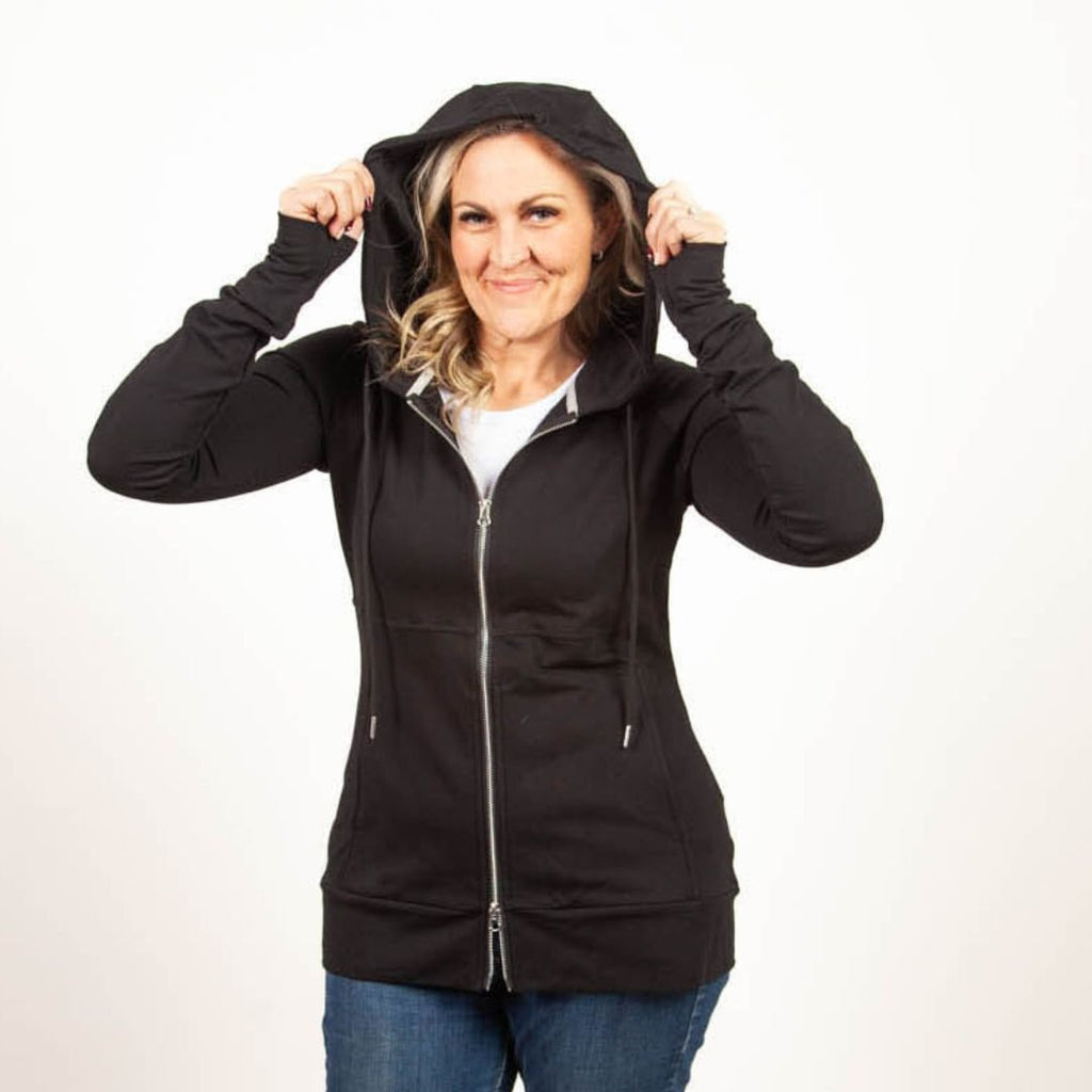 A woman wearing a black full-zip hoodie with a hood, thumbholes, and long sleeves. shown in size medium