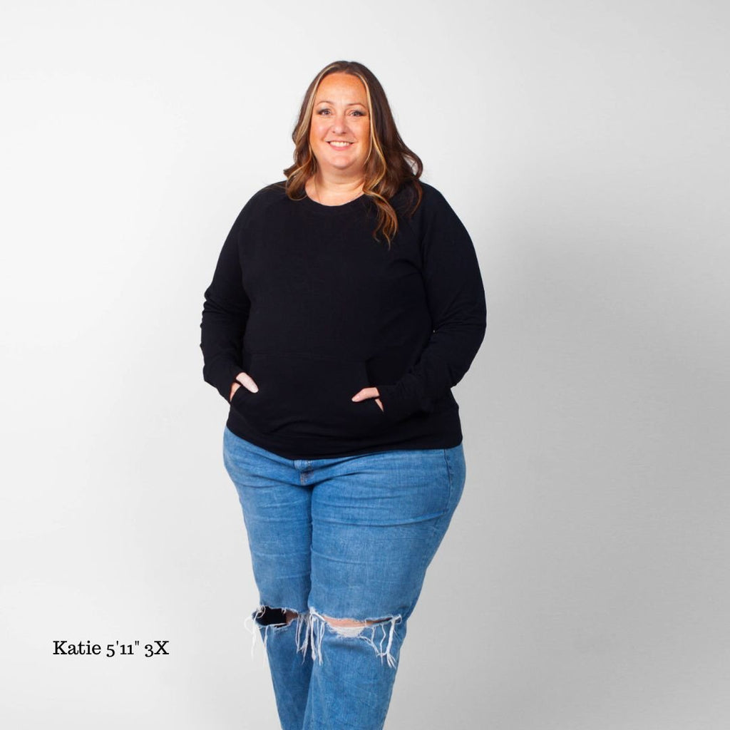 A woman wearing a long-sleeve black crew neck with thumbholes and kangaroo pocket. shown in size 3X