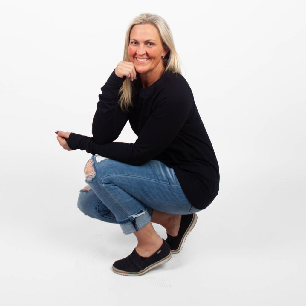 A woman wearing a long-sleeve black crew neck with thumbholes and kangaroo pocket. shown in size medium