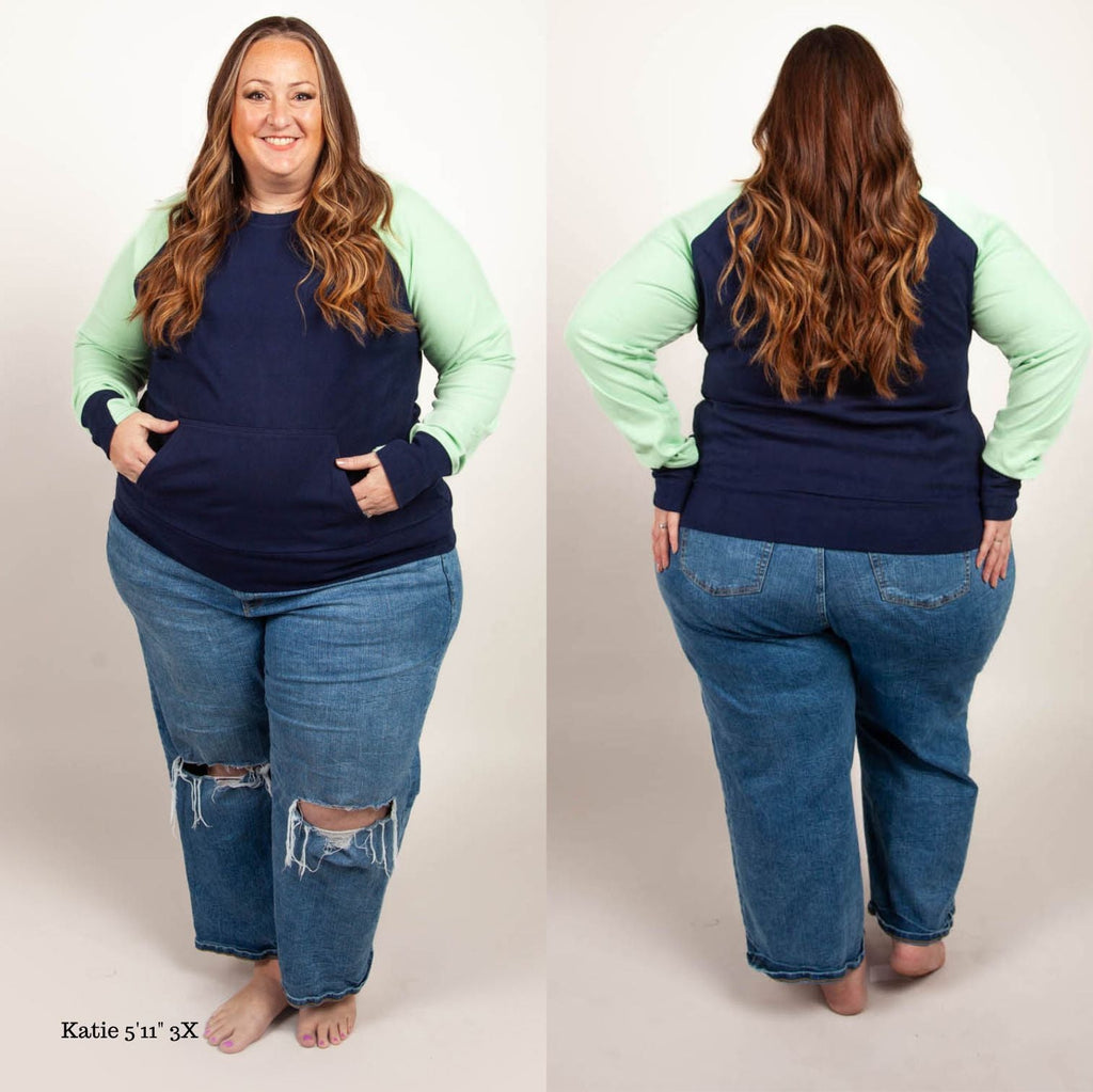 A woman wearing a long-sleeved crew neck pullover with a kangaroo pocket, in blue and green colors, with thumbholes. shown in size 3XL