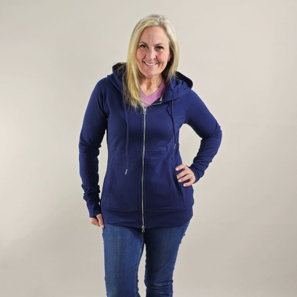 A woman wearing a navy full zip hoodie with a hood, thumbholes, and pockets. shown in size medium