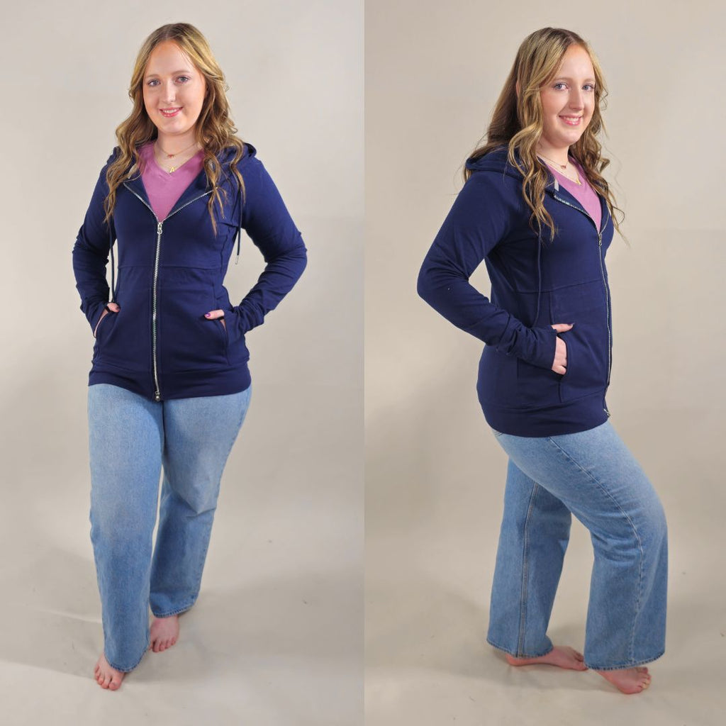 A woman wearing a navy full zip hoodie with a hood, thumbholes, and pockets. shown in size medium