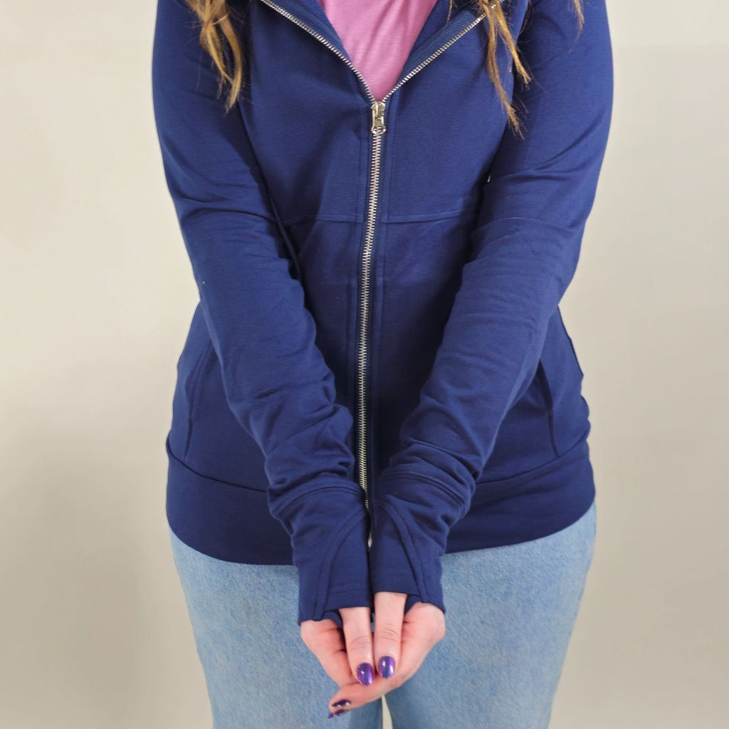 A woman wearing a navy full zip hoodie with a hood, thumbholes, and pockets.