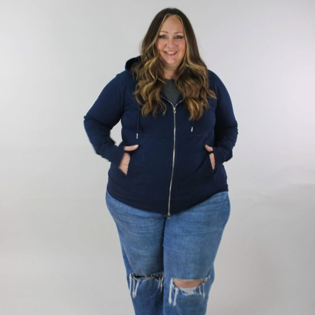 A woman wearing a navy full zip hoodie with a hood, thumbholes, and pockets. shown in size 3XL