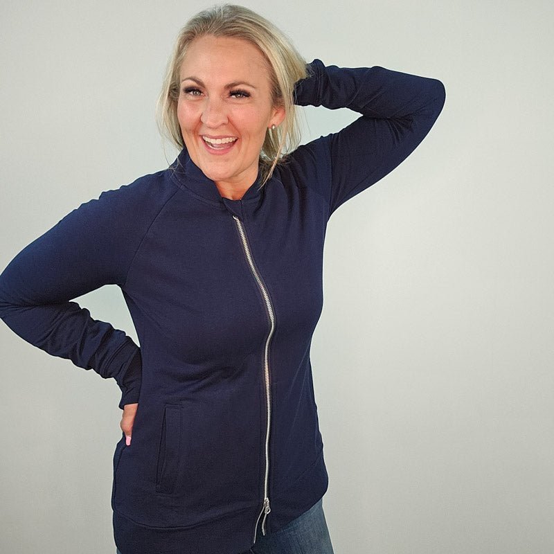 A woman wearing a navy blue hoodless jacket with a stand collar, full front zipper, and thumbholes. shown in size medium