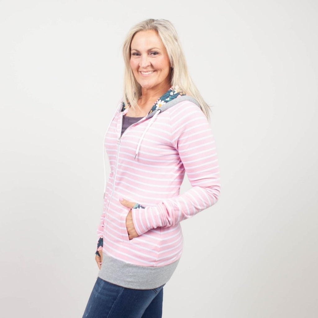 Woman wearing a pink striped hoodie with a floral lined hood, thumbholes, and double zipper. shown in size medium