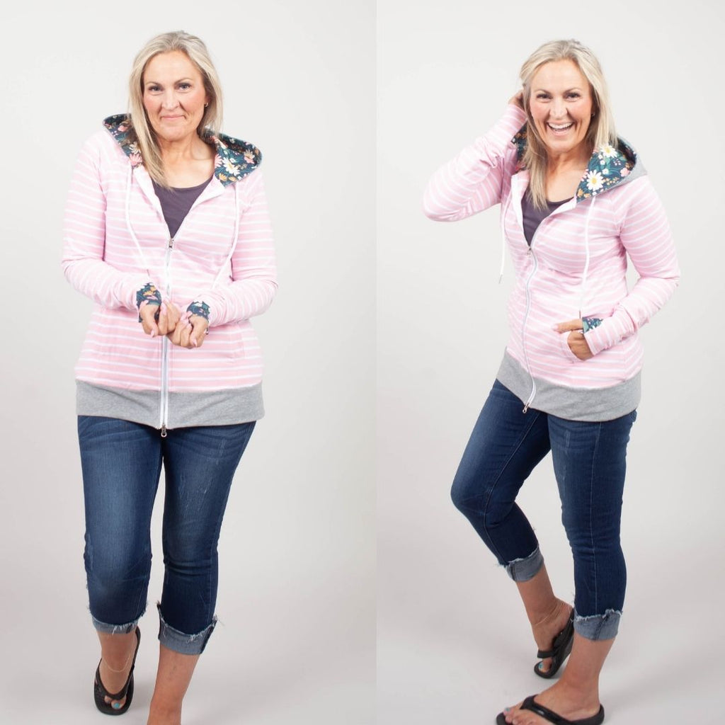 Woman wearing a pink striped hoodie with a floral lined hood, thumbholes, and double zipper. shown in size medium